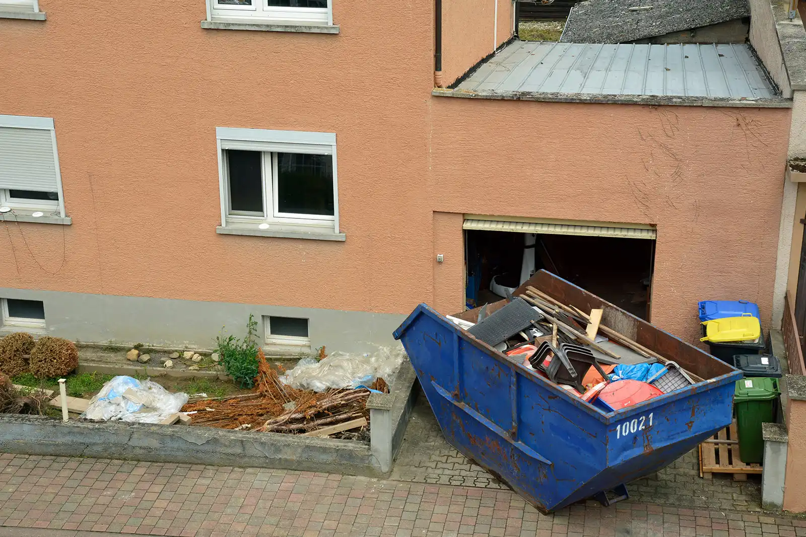 Container voller Gerümpel steht vor einem Haus